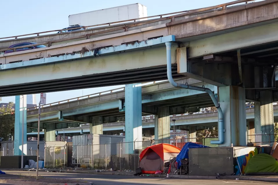 Tents set up against fence by unhoused people under freeway overpass in San Francisco, California.